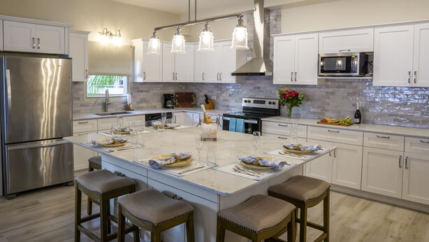 A modern kitchen with white cabinetry, a stainless steel refrigerator, a central island with bar stools, and a microwave above the counter.