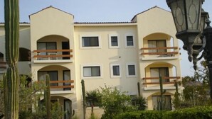 A multi-story building with balconies, surrounded by cacti and small trees.