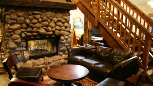 A stone fireplace, leather seating, and a wooden staircase in a cozy interior space. - Beautiful Donner Lake Home  (Truckee)