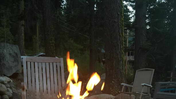 A fire pit surrounded by rocks and a bench in a wooded area. - Beautiful Donner Lake Home  (Truckee)