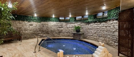 Ein Wellnessbereich mit Steinwand, Holzboden, einem kleinen Pool und einer Bank.