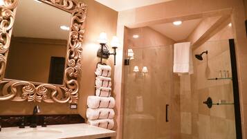 A bathroom with a large ornate mirror, a sink with a black faucet, and a glass-enclosed shower area with a towel rack.