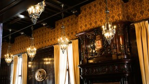 Une pièce ornée de lustres somptueux, d’une cheminée surmontée d’un blason et de papiers peints à motifs.