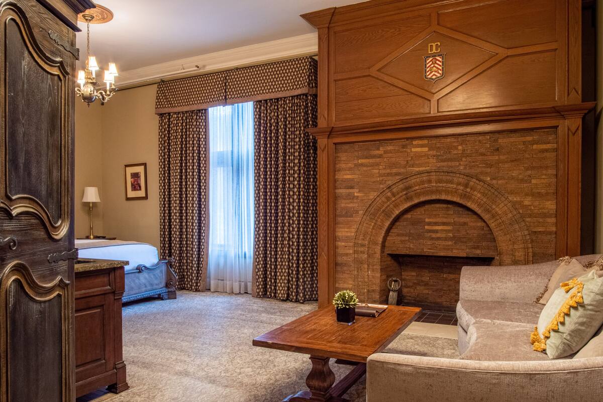 A hotel room with a wooden fireplace, a sofa, a coffee table, and a bed with curtains.