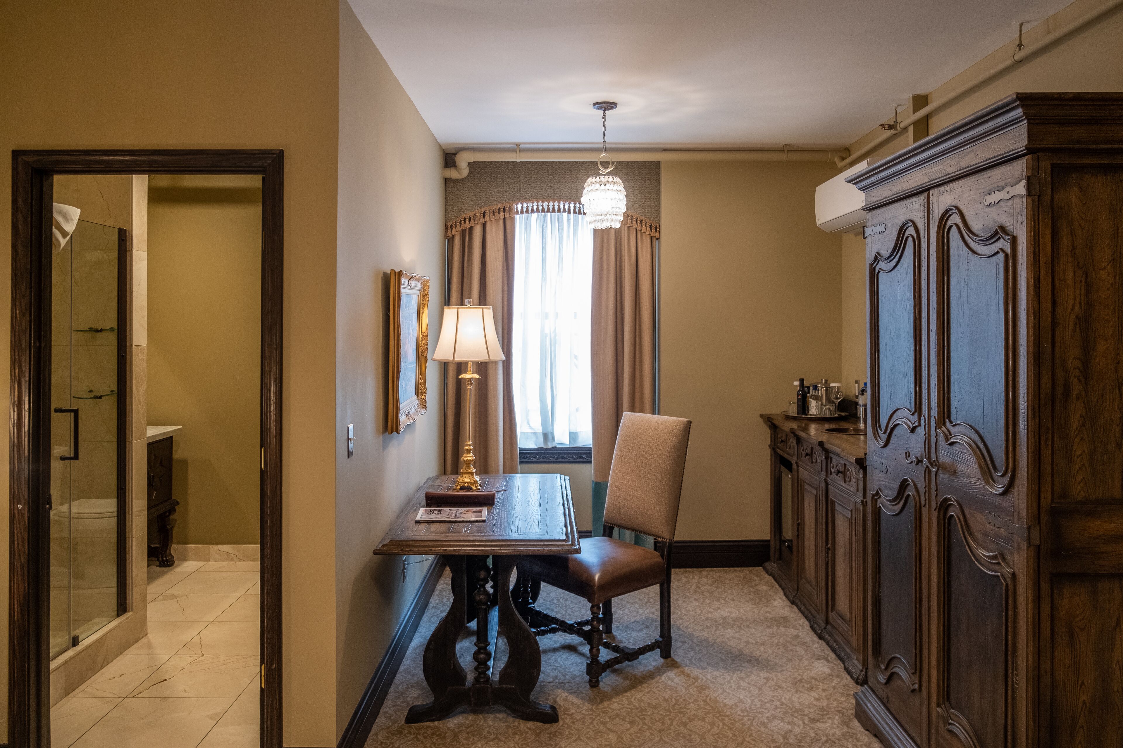 A room with a dining table, a chair, a chandelier, a cabinet, and a window with curtains.