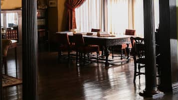 A dining area with a wooden table and chairs, a large window with curtains, and a green wall.