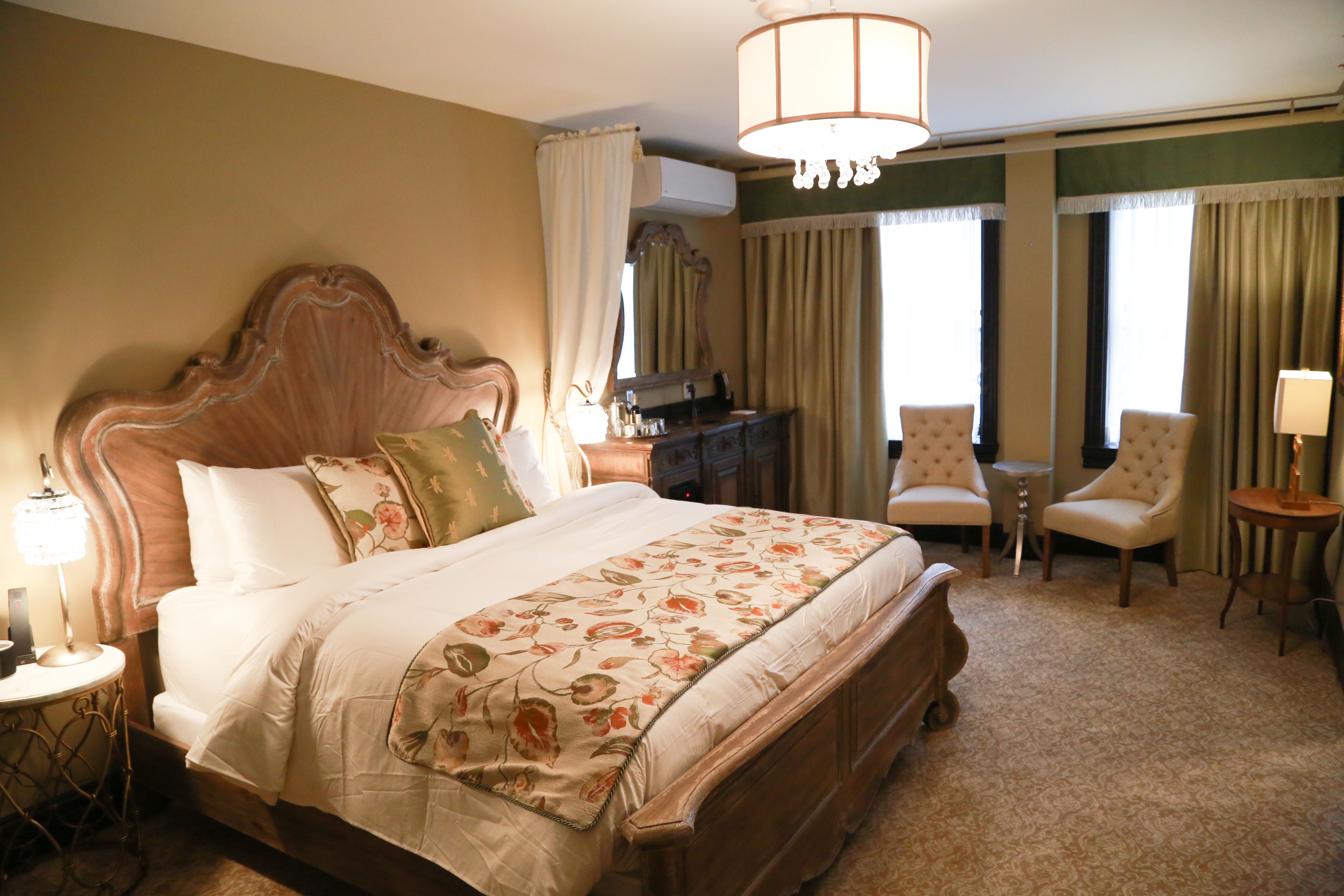 A spacious hotel room with a large bed, two armchairs, a small table, and a desk.