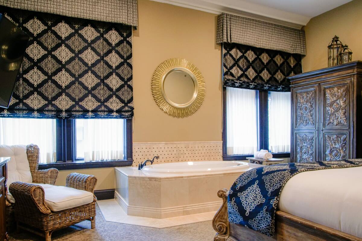 A spacious bathroom with a large bathtub, a mirror, and a wicker chair.