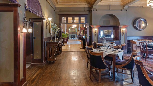 Une salle à manger élégante, dotée d’un parquet en bois, de chaises à revêtement sombre et d’un lustre.