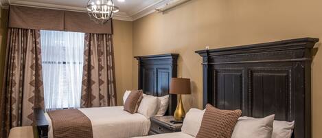 A hotel room with two beds, a chandelier, a fireplace, and a window with curtains.