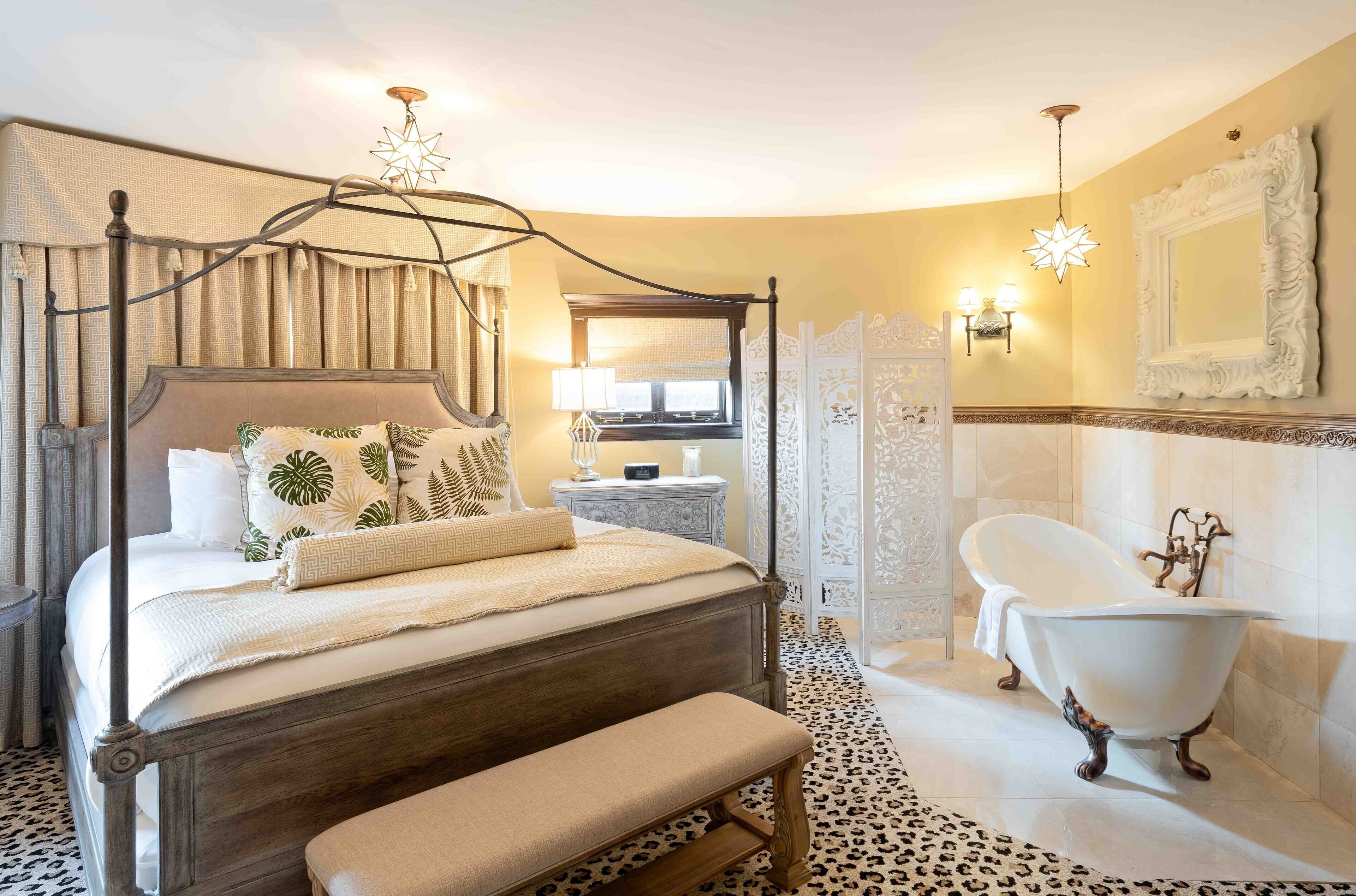 Una cama con dosel, un banco, una bañera de patas de león y un espejo grande con marco decorativo.