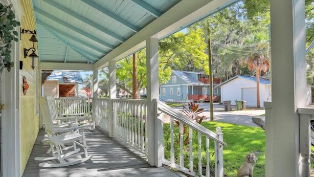 A covered porch with white railings, a rocking chair, and a small statue.