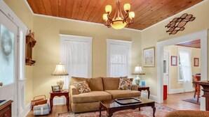 A cozy living room with a wooden ceiling, a beige sofa, a coffee table, and a patterned rug.