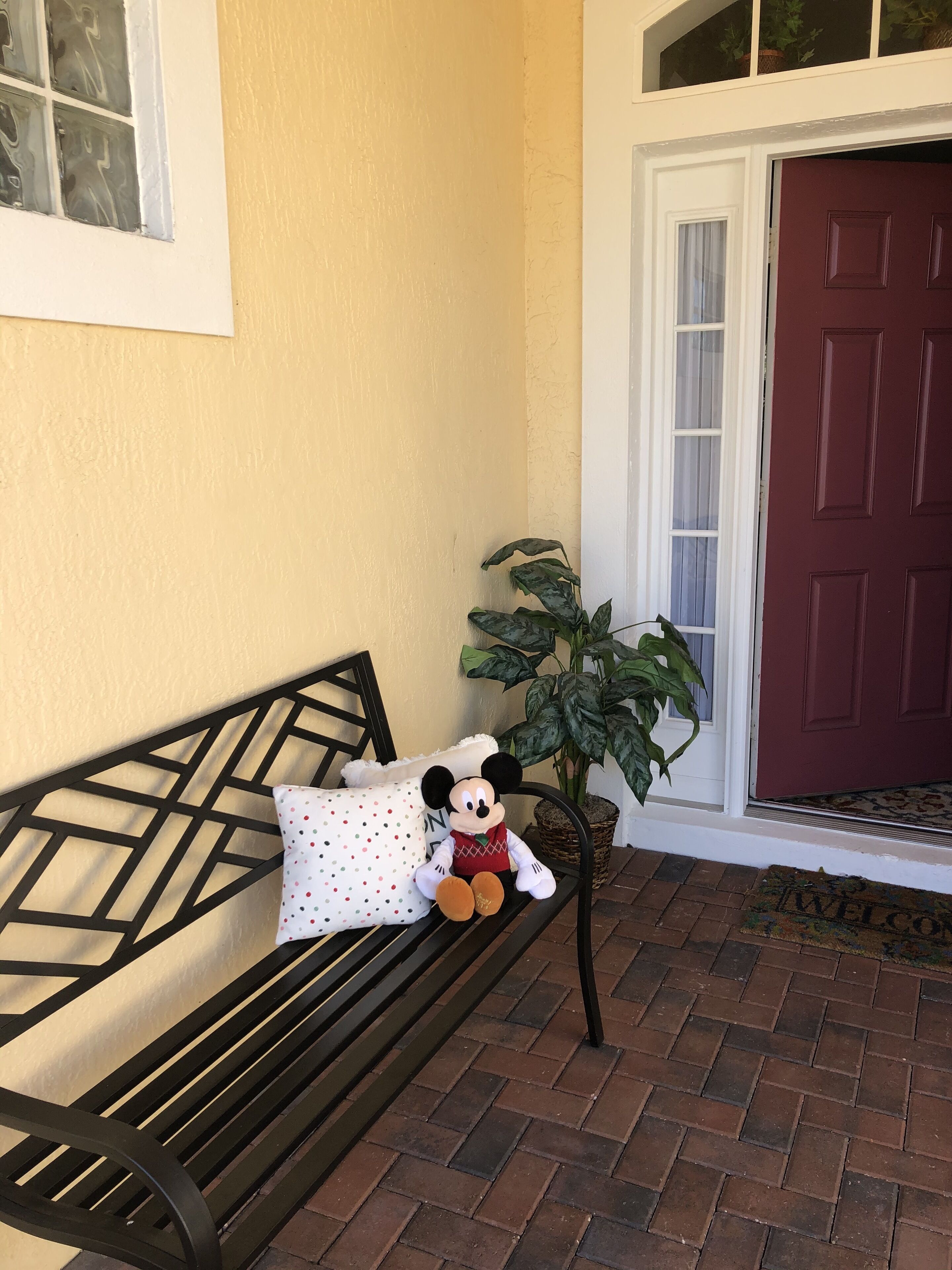 Een bank met een Mickey Mouse knuffel, een stippen kussen en een bloempot met plant.