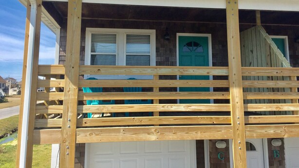 Une terrasse en bois avec une balustrade blanche, une porte verte et une porte de garage blanche.