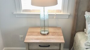 Une table de chevet avec une lampe, un tiroir et une fenêtre avec des stores.