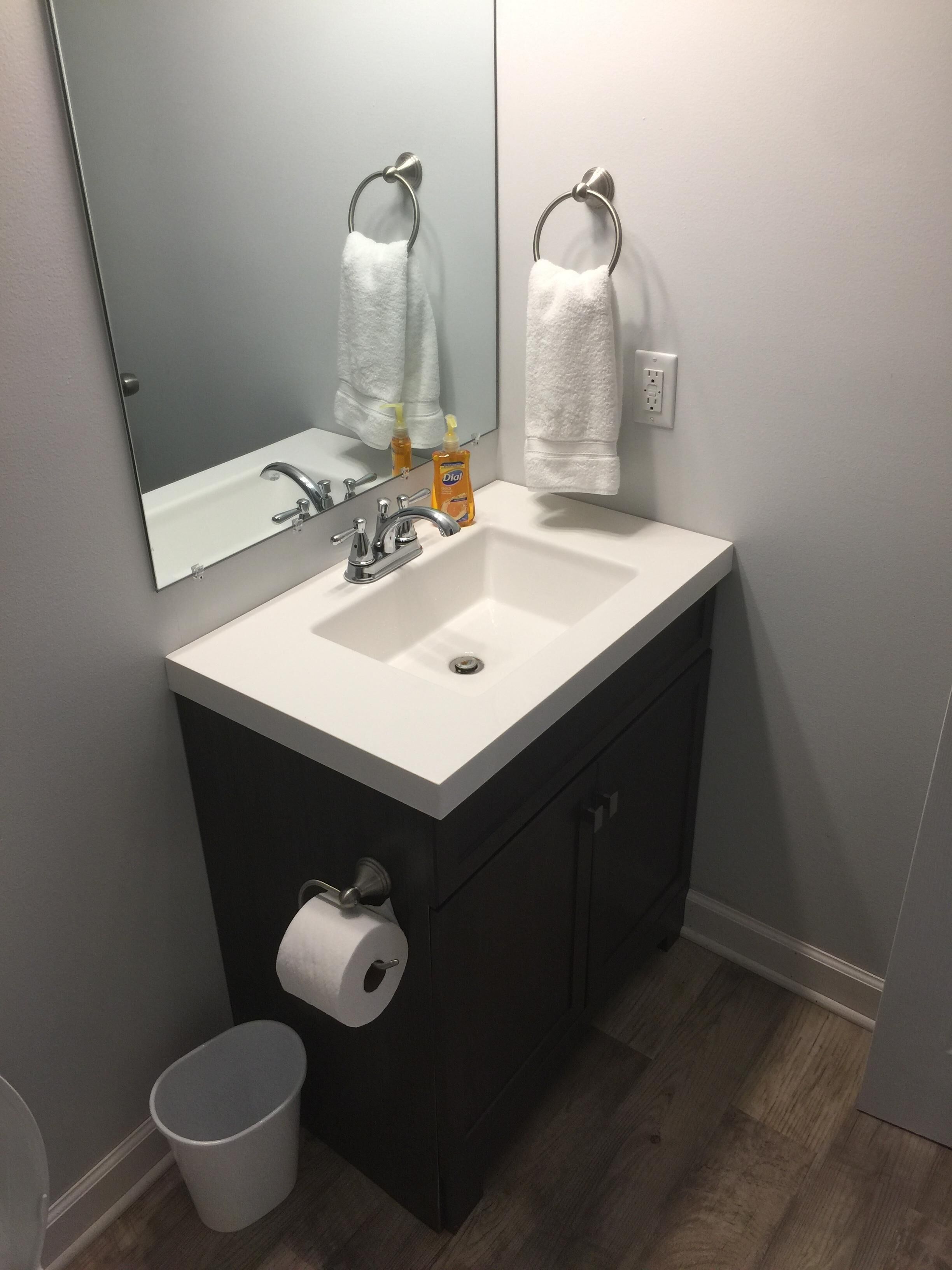 Une salle de bain avec un lavabo blanc, des meubles sombres, un miroir et une serviette accrochée au mur.