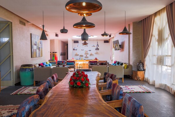 Un vaste espace dédié à la salle à manger, avec une longue table en bois, de nombreuses chaises et un arrangement floral central.