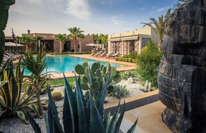 A pool area with lounge chairs, cacti, and a rock wall.