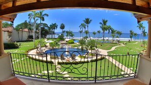 A balcony with a view of a pool, palm trees, and the ocean.