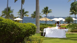 A person receiving a massage outdoors with palm trees and a view of the ocean.