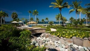 A tropical resort with palm trees, a pool area, and a view of the ocean.