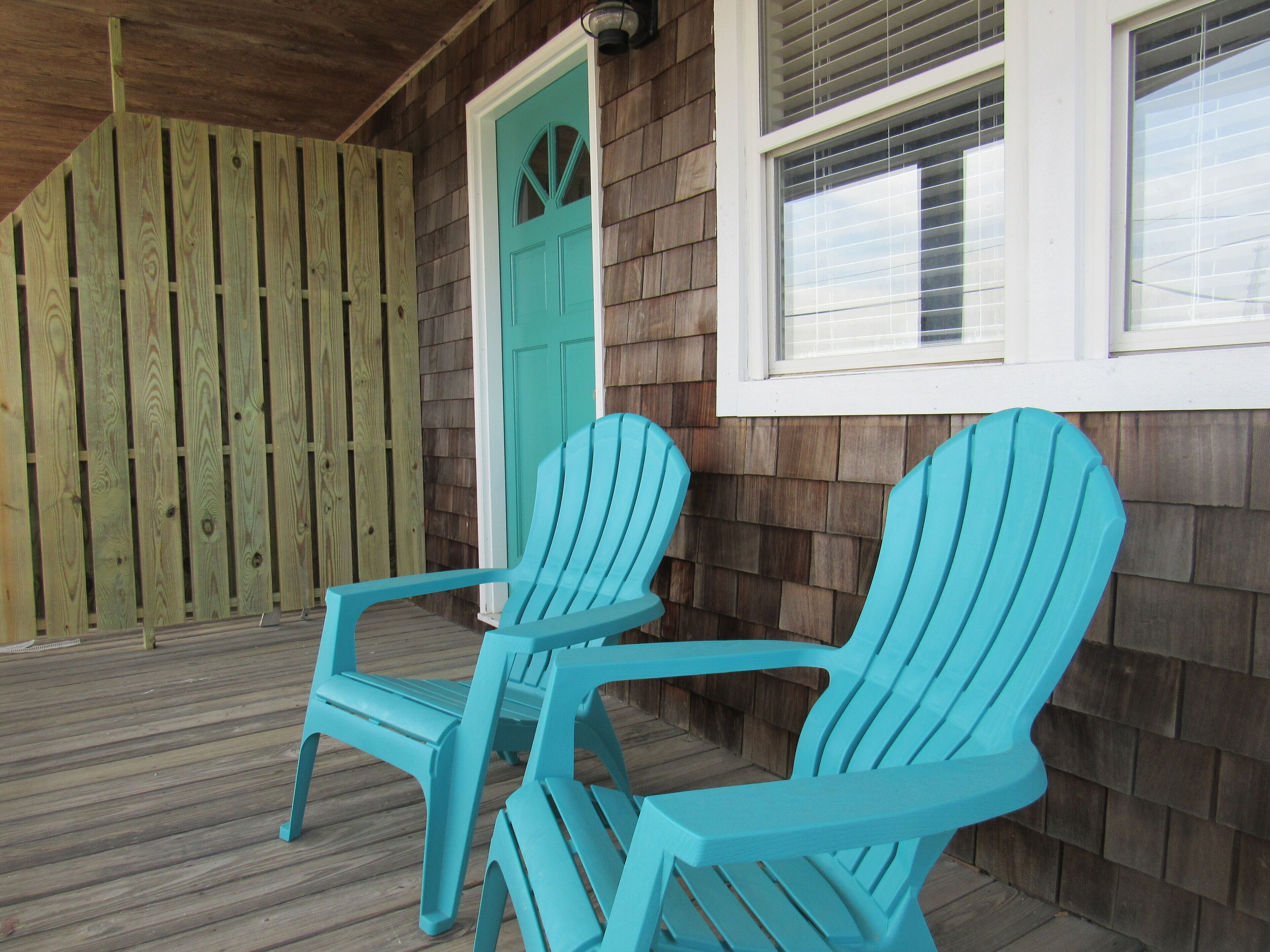 Een houten terras met twee turquoise Adirondack-stoelen en een turquoise deur.