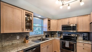 Una cocina moderna con armarios de madera, electrodomésticos de acero inoxidable, encimera de granito y una ventana con persianas.