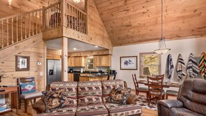 A spacious living area with a wooden staircase, a kitchen, and a dining area. - Creekfront Cabin | Hot Tub | 1GB WiFi | Gated | Pets Welcome (Maggie Valley)