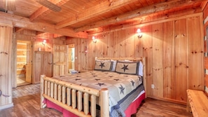 A wooden cabin-style bedroom with a bed, a bench, and a door leading to another room.