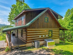 A rustic cabin with a porch, a chimney, and a small attached shed.