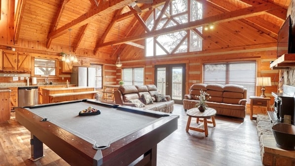 A spacious wooden cabin with a pool table, a sofa, and a fireplace.