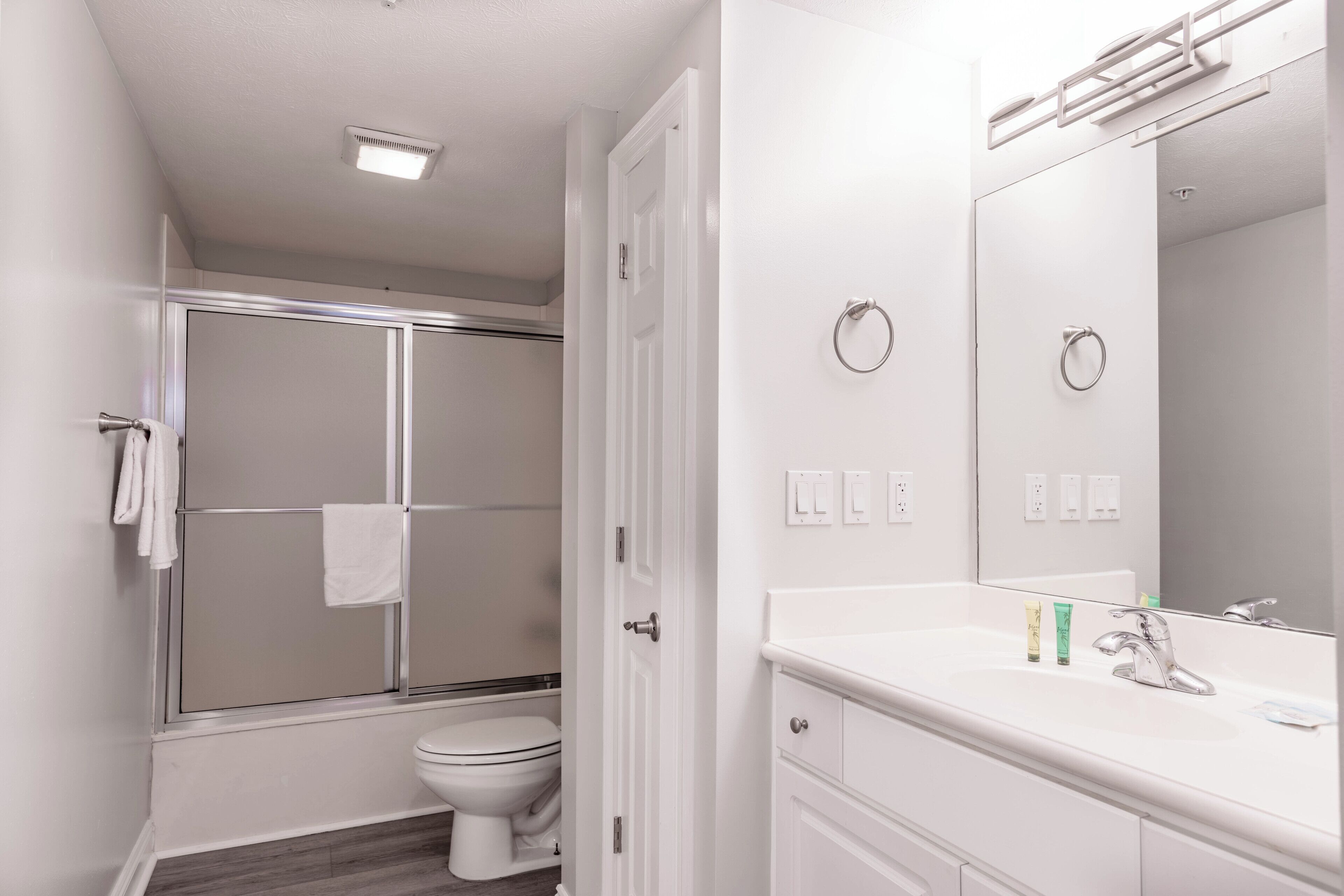 Ein modernes Badezimmer mit Duschkabine aus Glas, Toilette, Waschbecken mit Spiegel und Handtuchhalter.