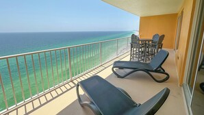 A balcony with a view of the ocean, a table with chairs, and two lounge chairs.