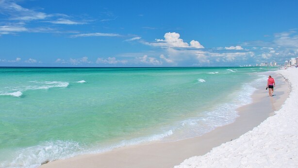 A beach with clear turquoise water, a sandy shore, and a distant city skyline.