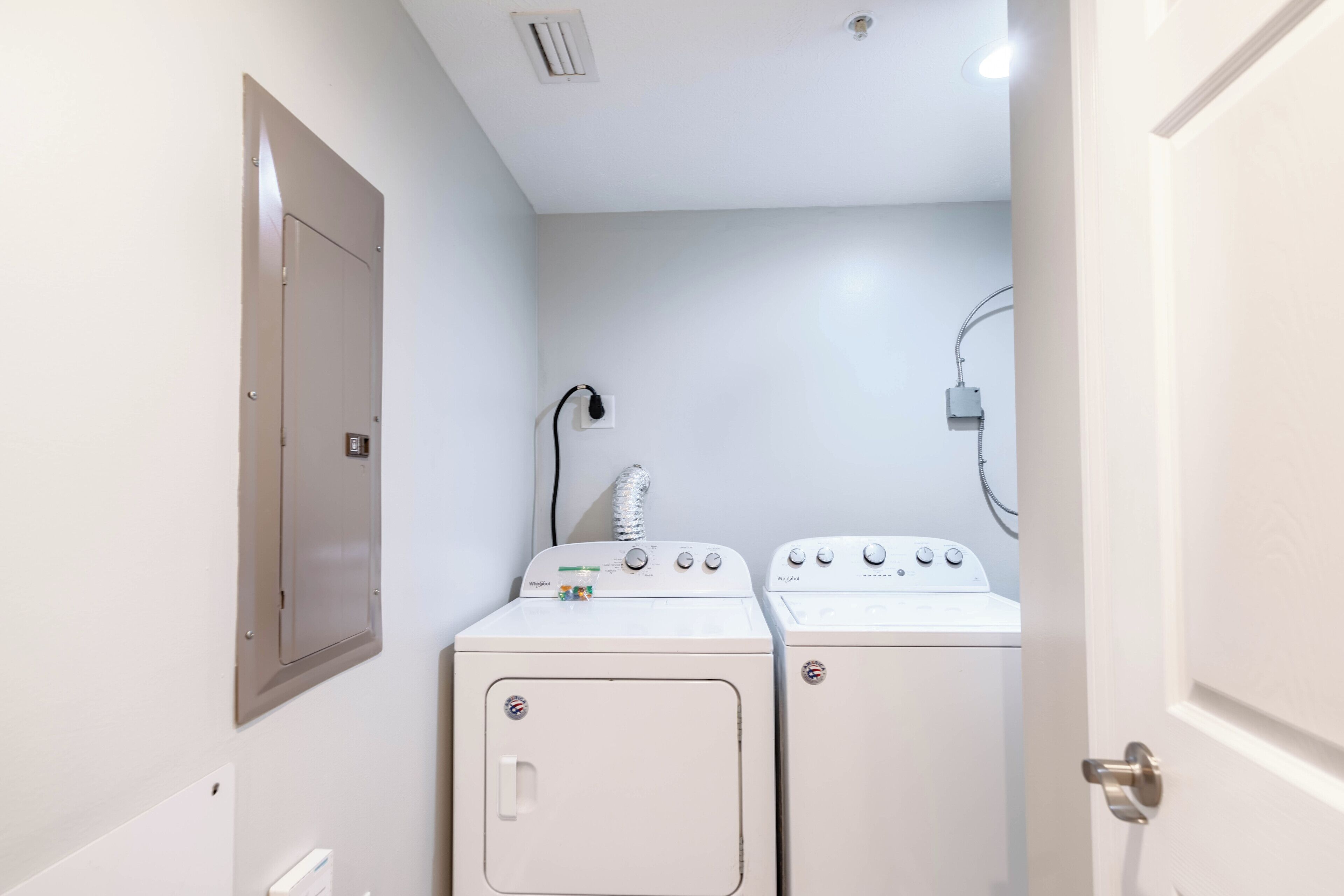 A laundry room with two white washing machines and a dryer, a vent, and a door.