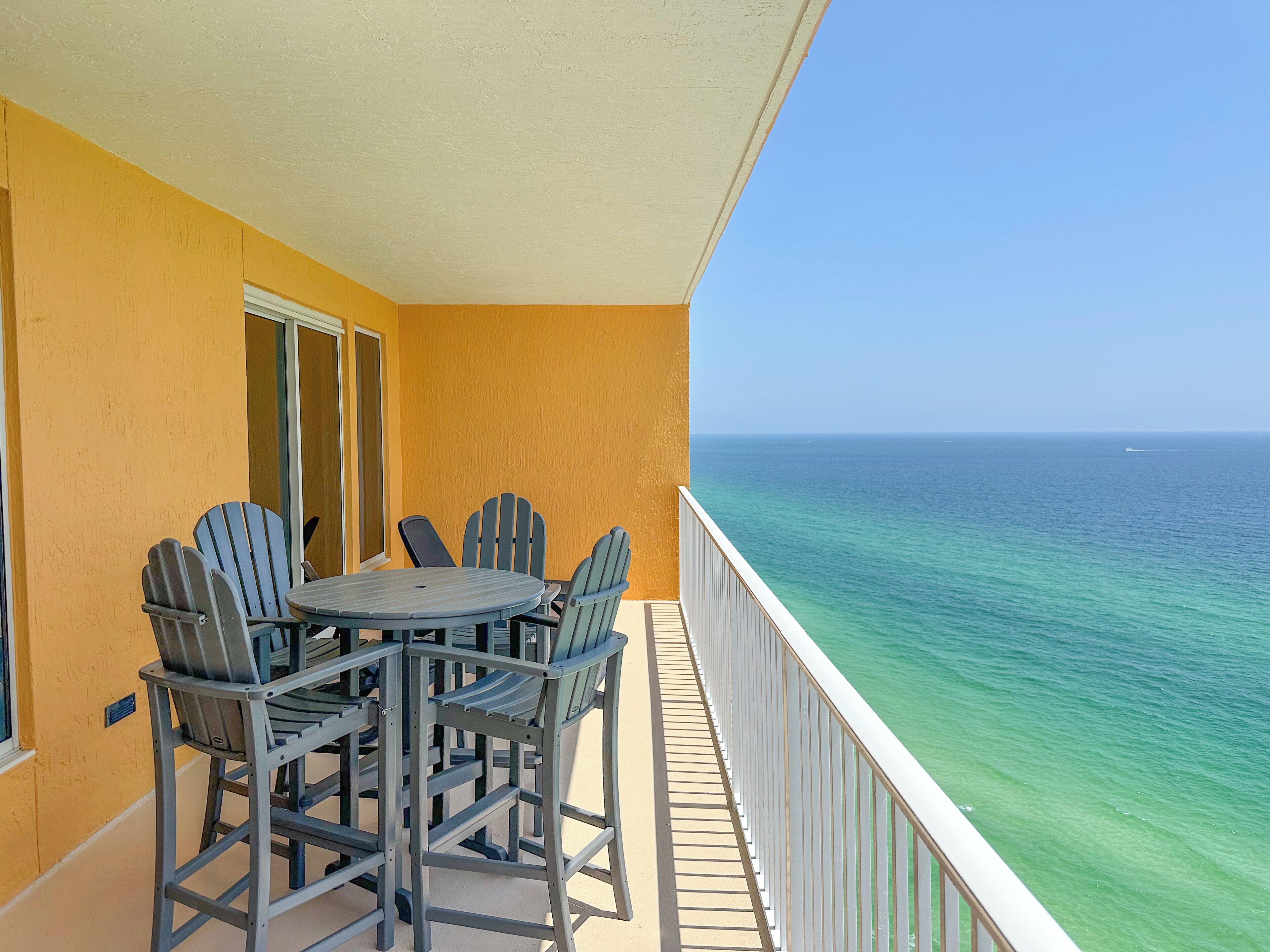 A balcony with a table and chairs, overlooking a clear ocean view.