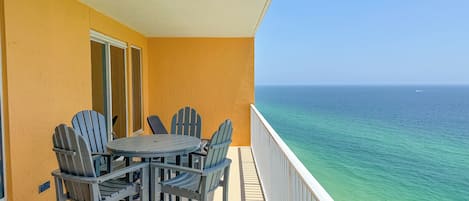 A balcony with a table and chairs, overlooking a clear ocean view.