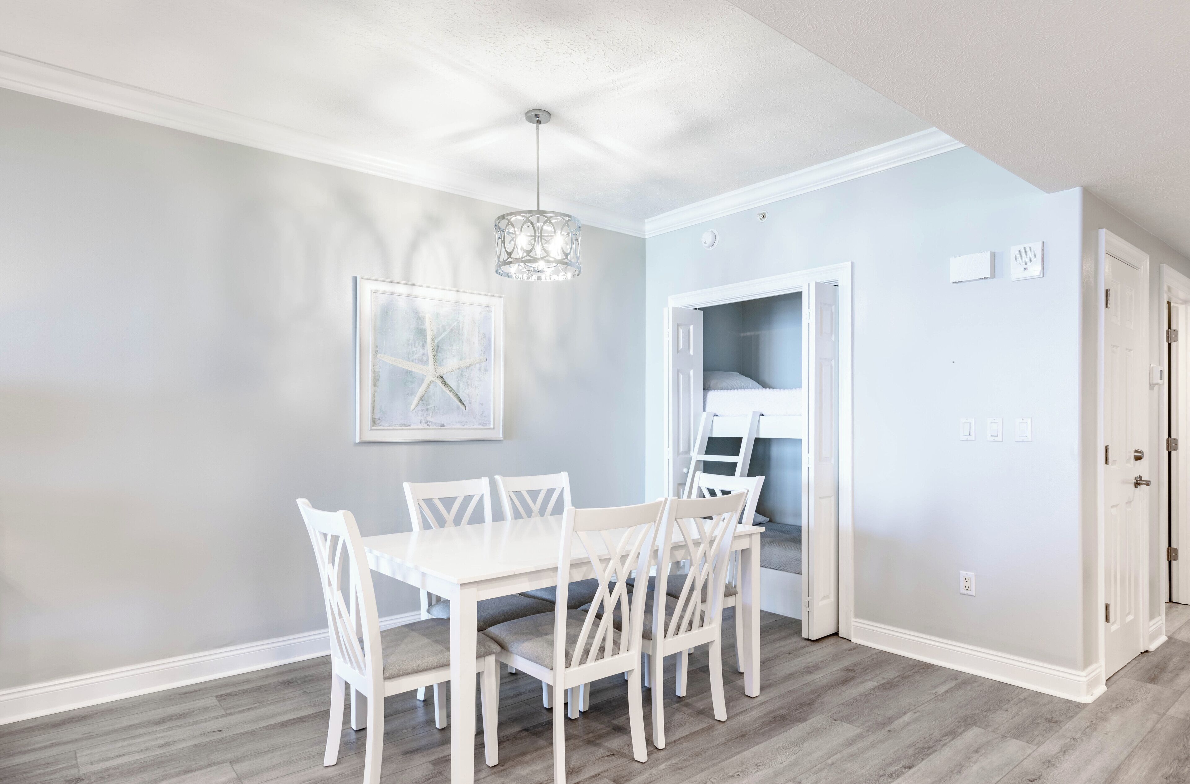 A dining area with a white table and chairs, a chandelier, and a door leading to a closet.