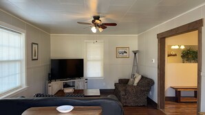 Ein Wohnzimmer mit Fernseher, Sofa und Deckenventilator. Es gibt einen Essbereich mit Tisch und Stühlen.