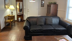 Ein Wohnzimmer mit einem schwarzen Ledersofa, einem Holznachttisch mit Lampe, einem Holzkabinett und einer Tür mit Buntglasfenster.