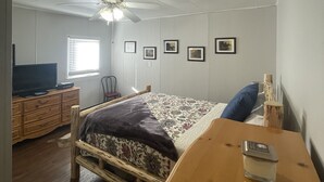 Ein Schlafzimmer mit Bett, einem Holzschrank, Fernseher, Deckenventilator und gerahmten Bildern an der Wand.