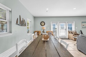 A dining area with a long wooden table, two sofas, a lamp, and a wall clock. - Beautiful Home with Direct Beach Access (Gulf Shores)