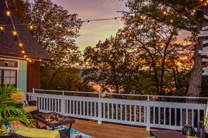 A wooden deck with a white railing, string lights, and outdoor furniture. - On the Rocks Cottage. Lakefront, Dog-Friendly. Sleeps 16. Bunkhouse. Free Wifi (Eagle Rock)