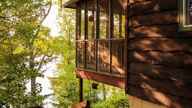 Une cabane en bois dotée d’un balcon donnant sur une zone boisée.
