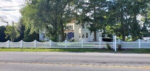 A two-story house with a white picket fence, surrounded by trees.