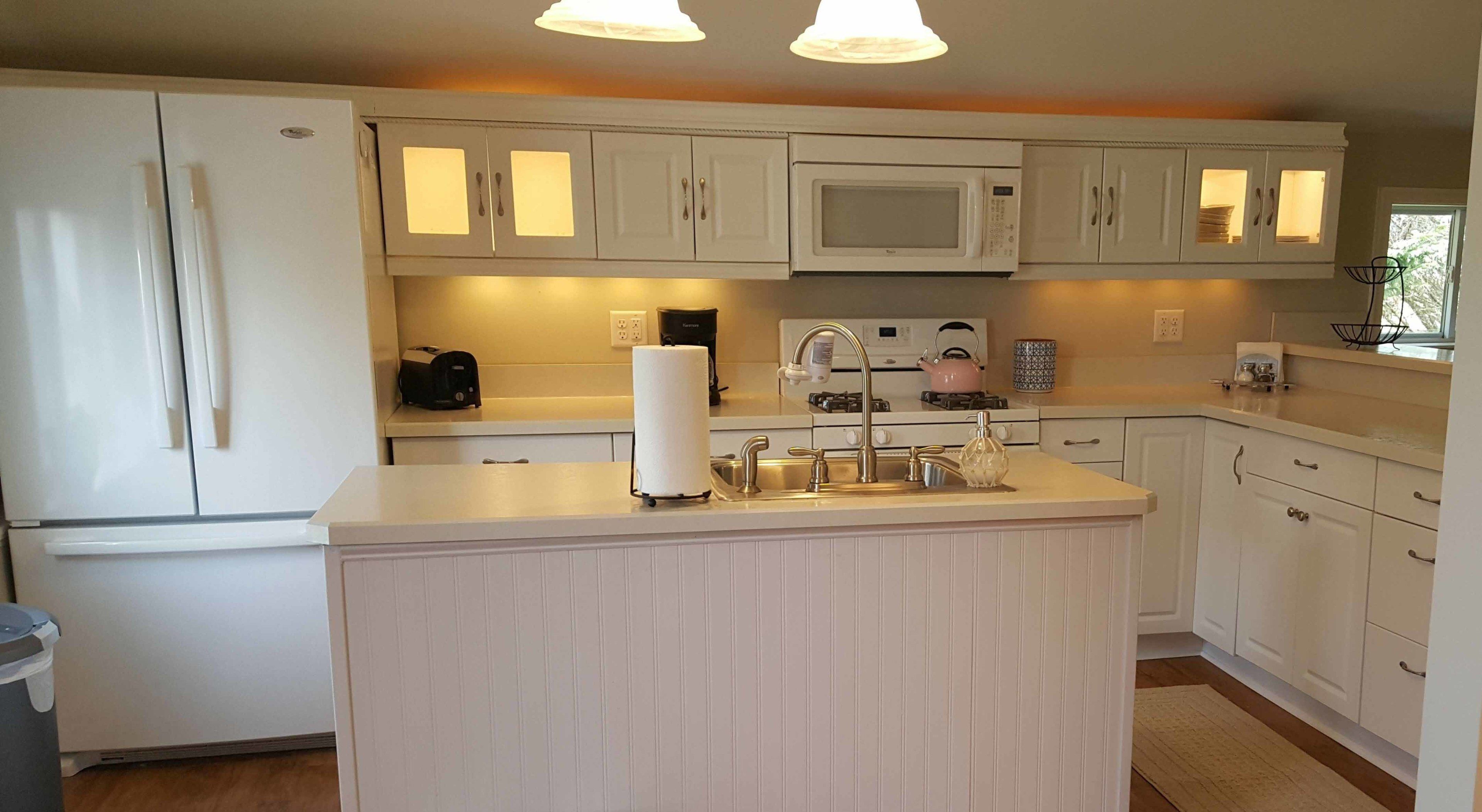 A kitchen with white cabinets, a central island with a sink, a microwave, and a gas stove.