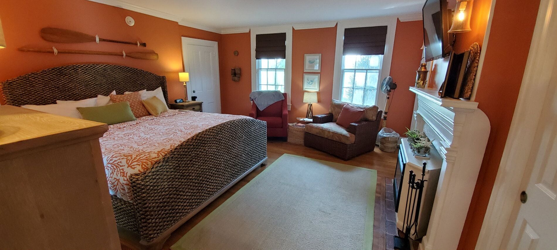 A cozy bedroom with a large bed, a red armchair, a small sofa, and a fireplace.