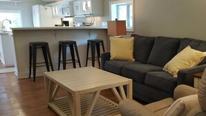 Un saló modern amb un sofà gris, dos coixins grocs, una taula de centre de fusta i tamborets negres.