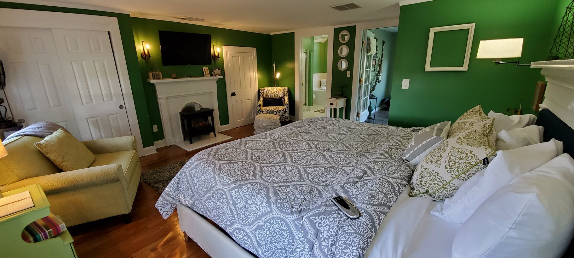 A bedroom with a large bed, a chair, a fireplace, and a green wall.